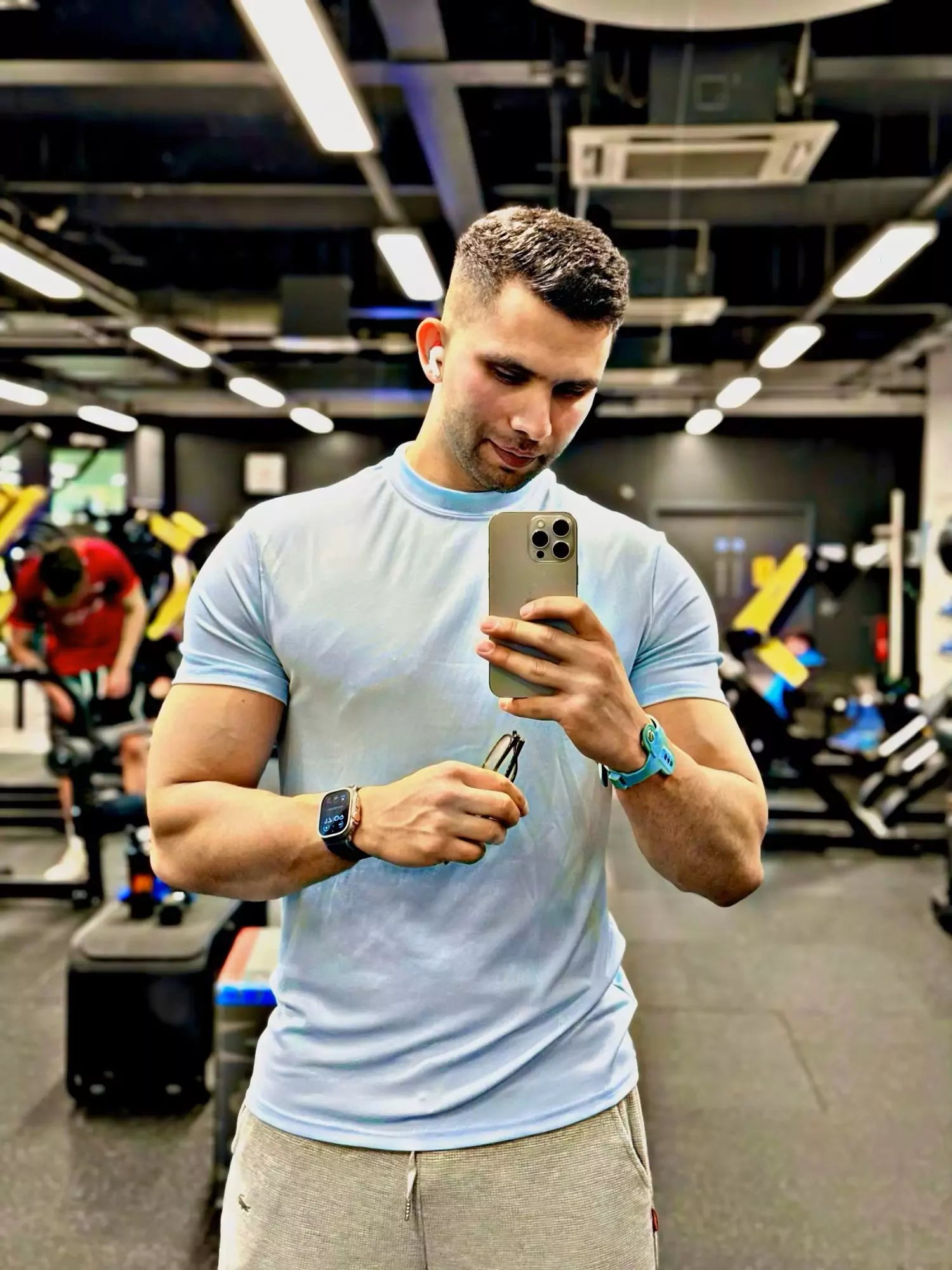 Man taking a selfie in a gym holding a phone and a water bottle.
