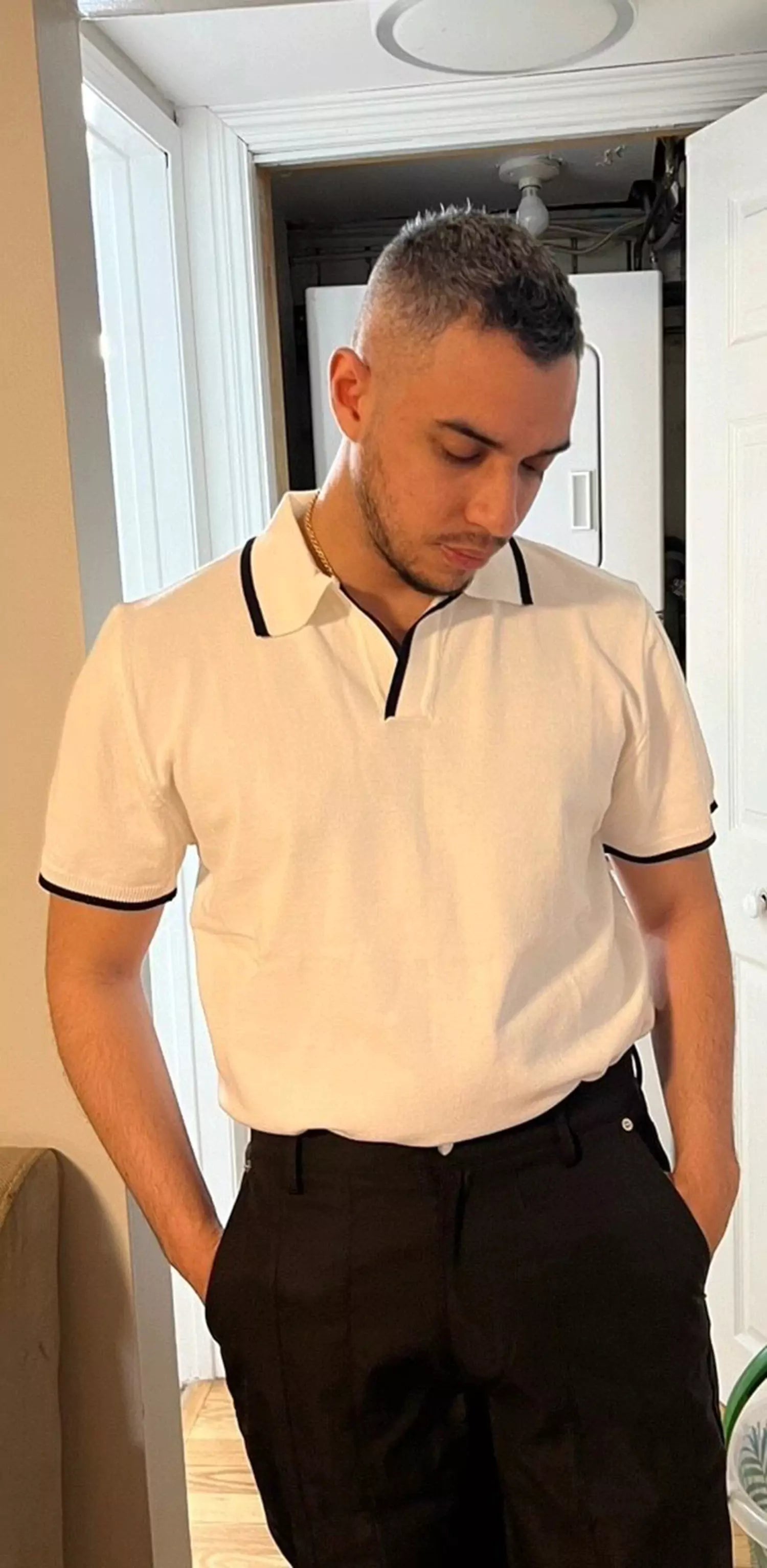 Man wearing a white polo shirt with black trim and black pants indoors.