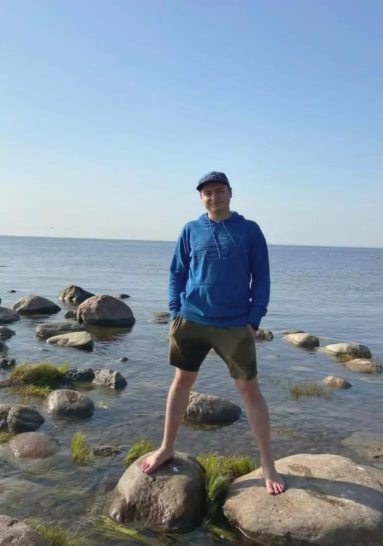 Person standing on rocks by a body of water with a clear sky